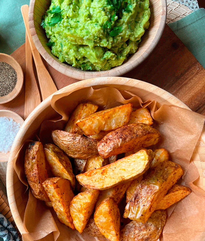 Papas rústicas doradas con piel, sazonadas con paprika y servidas con guacamole.