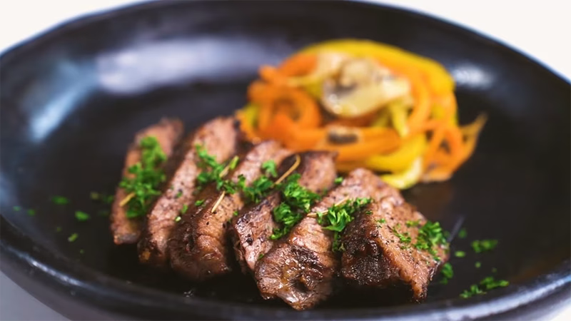 Trozos de res confitada con costra dorada y jugosa, acompañada de tiras de zucchini.