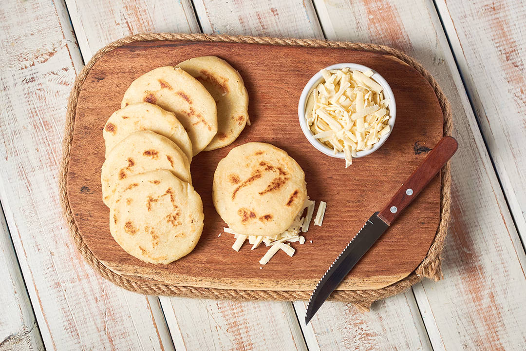 Bandeja de madera con arepas paisas acompañadas de queso rallado.