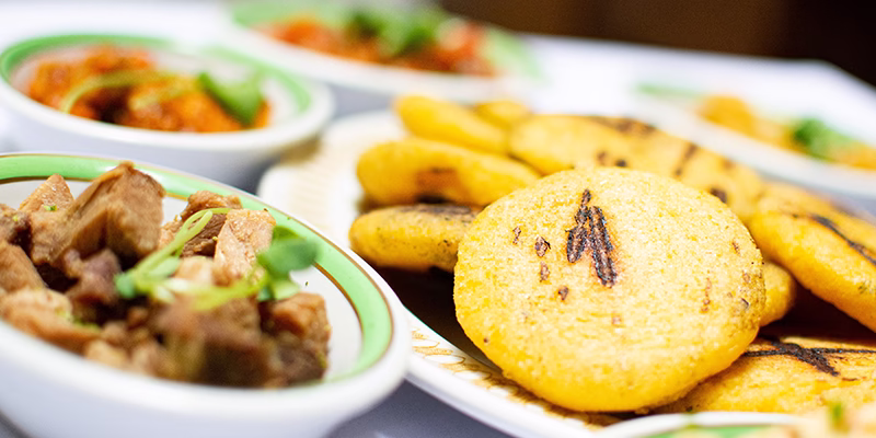 Arepas de maíz sobre un plato blanco, acompañadas con diferenes bowls con toppings como chicgarrón y hogao