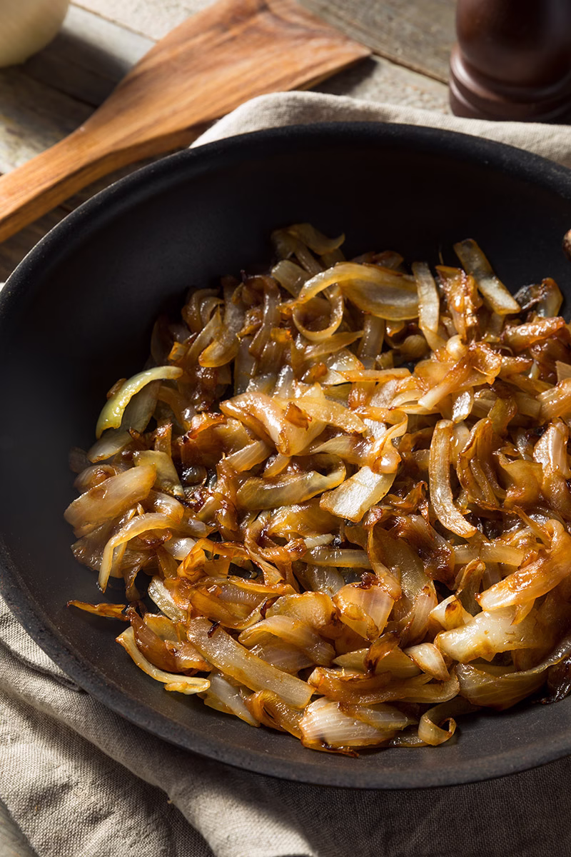 Cebolla cortada en julianas caramelizándose en un sartén negro.