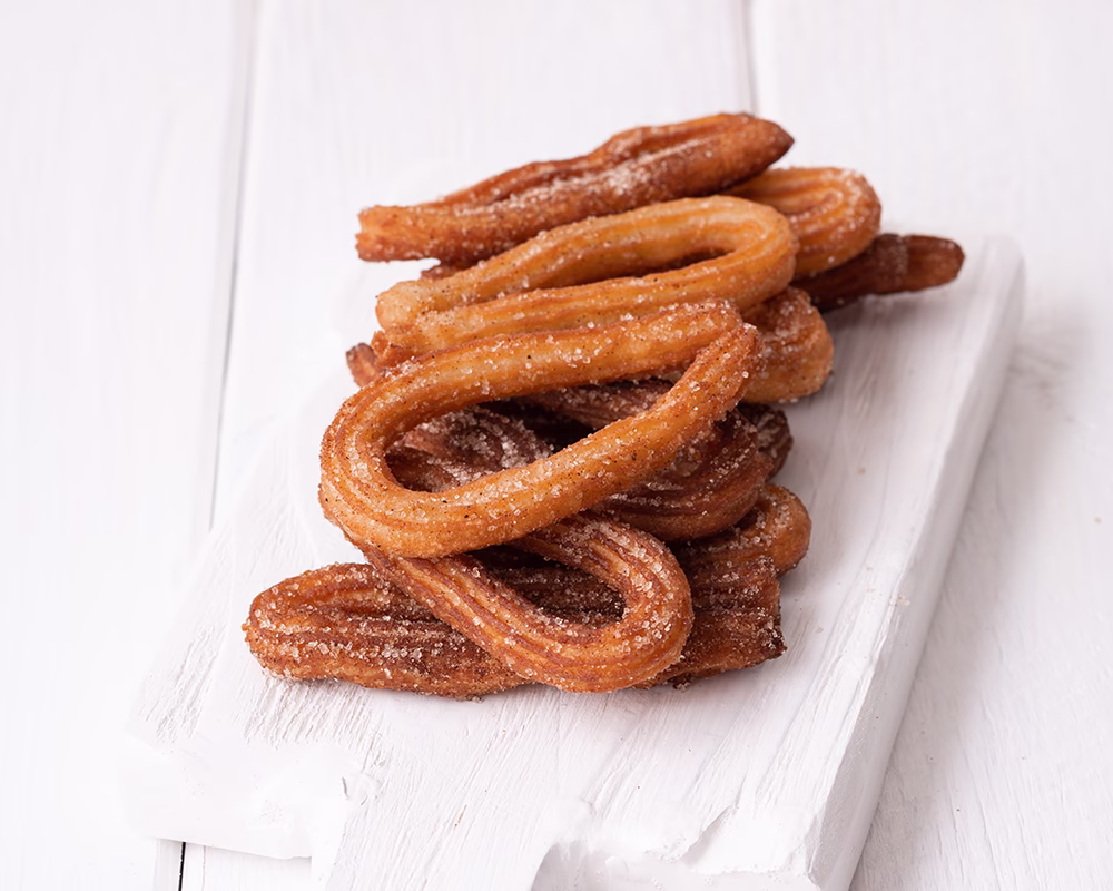 Vista de varios churros servidos sobre una tabla blanca de madera