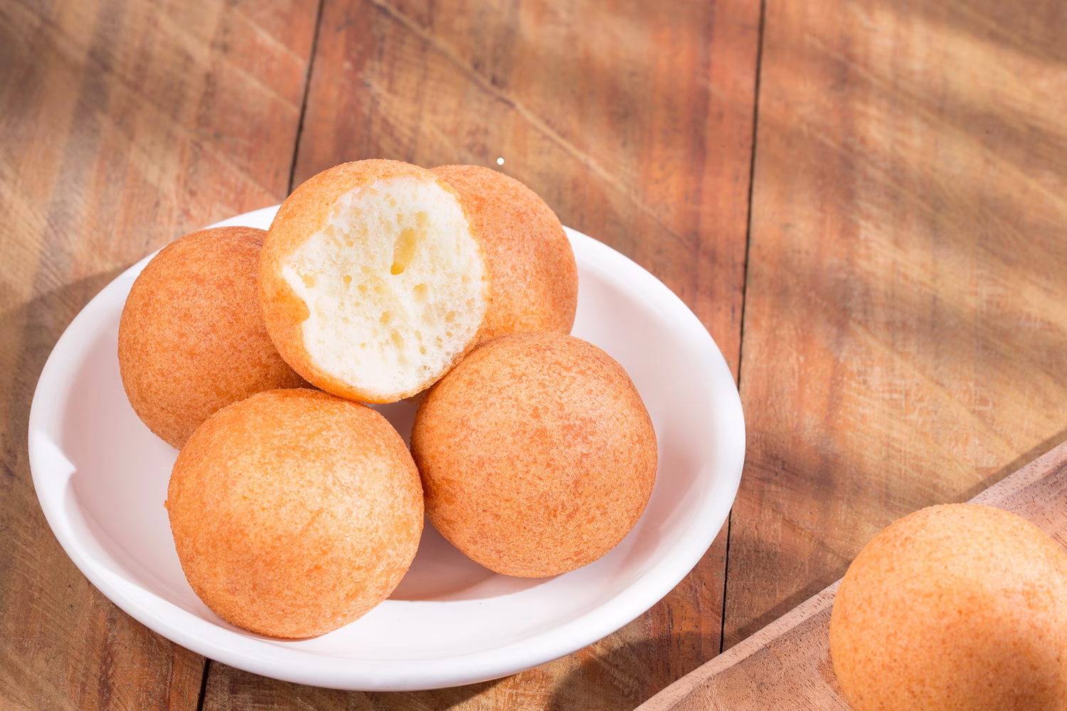 Buñuelos en un plato pequeño blanco sobre una mesa de madera.