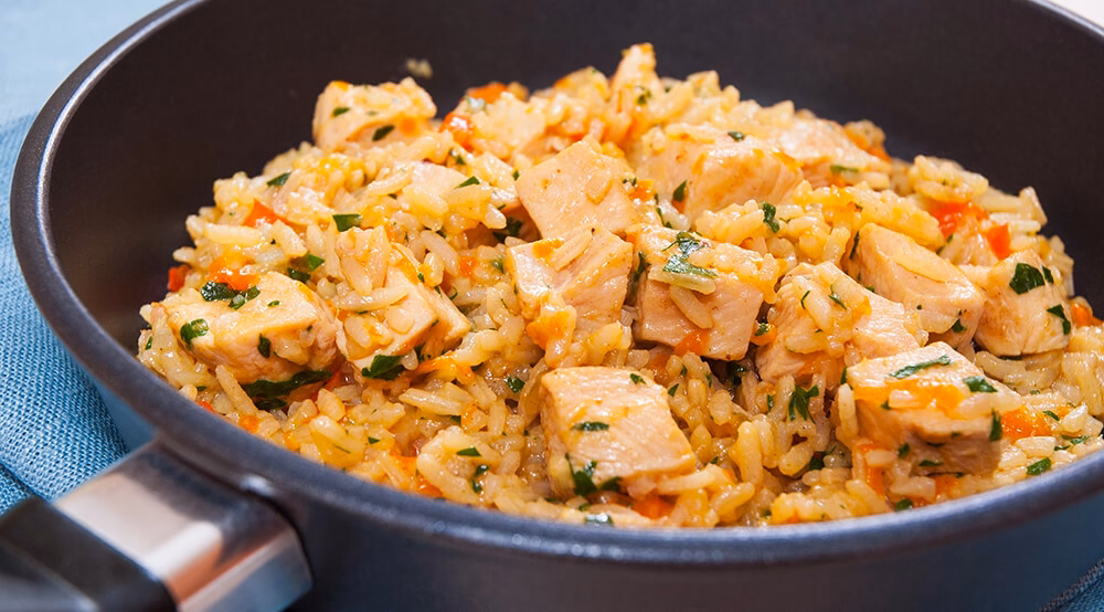 Vista detallada de plato de arroz con pollo sobre sartén en mesa con mantel azul aguamarina.