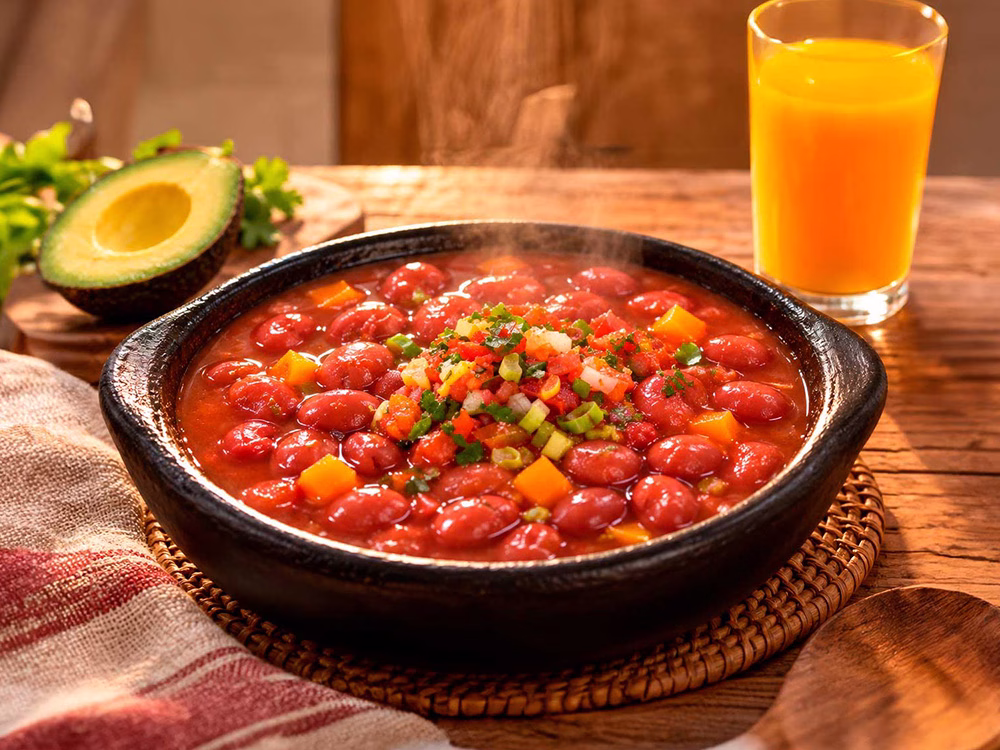Plato de fríjoles rojos con verduras picadas, acompañado de aguacate y jugo de naranja.
